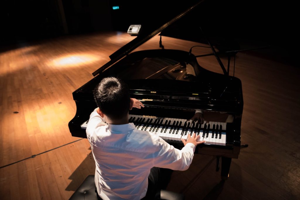 back view photo of a man playing a black grand piano